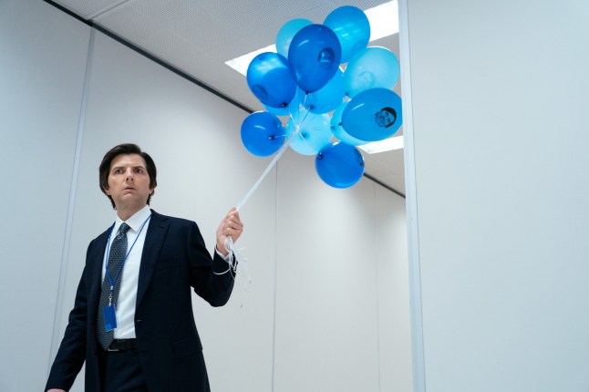 Adam Scott as Mark in Severance, holding some blue balloons while walking down a plain white corridor.