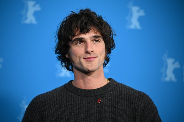Jacob Elordi posting against a blue background wearing black top